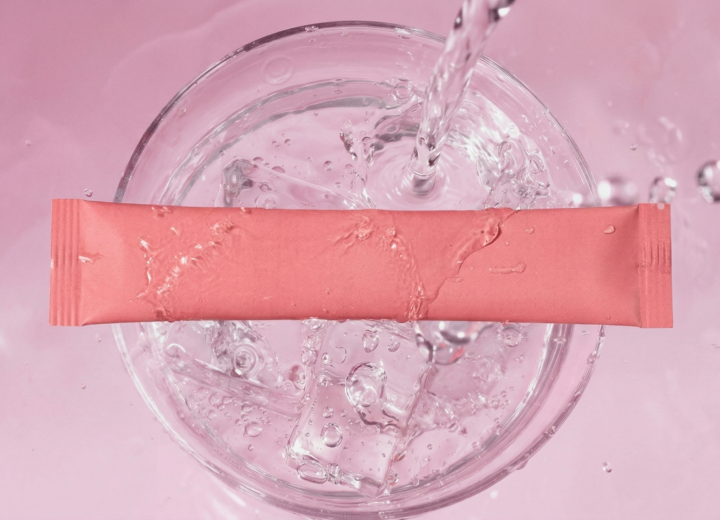 Electrolyte drink sachet with hyaluronic acid and collagen peptides over ice water.