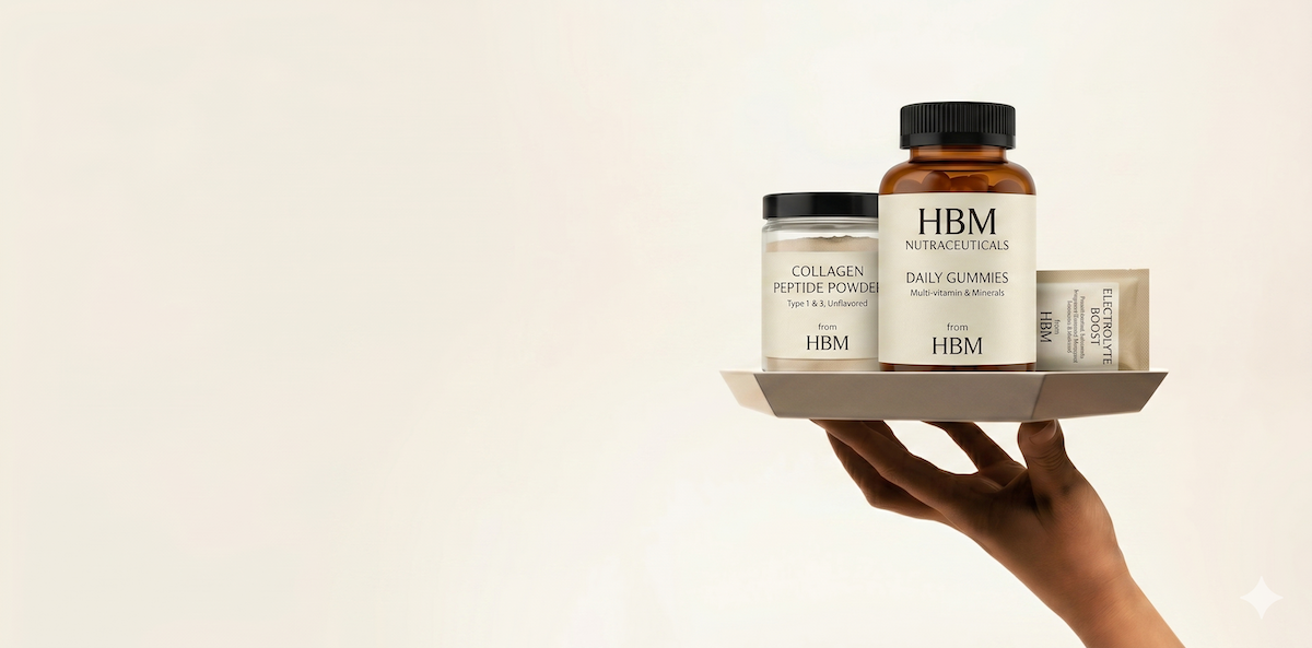 A hand holds a grey tray displaying three HBM Nutraceutical consumer behaviour trends in the supplement industry: a jar of unflavored Collagen Peptide Powder, a large bottle of Daily Gummy Vitamins, and a sachet of Electrolyte Boost. This high-end photo uses minimalist lighting to convey transparency to informed consumers.