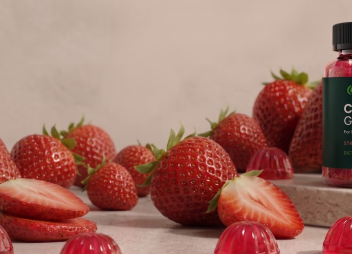 A high-quality product photograph of a bottle of green-labeled "Collagen Gummies" containing ingestible pink collagen gummies, surrounded by fresh whole and sliced strawberries to illustrate natural ingredients. This visual representation of a consumable supplement is part of a comparison discussion of collagen topical vs ingestible.